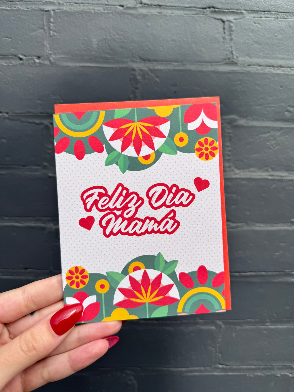 Spanish Mother's Day Card that says 'Feliz Dia Mama' with green, yellow and red flowers and shapes decorating the border.